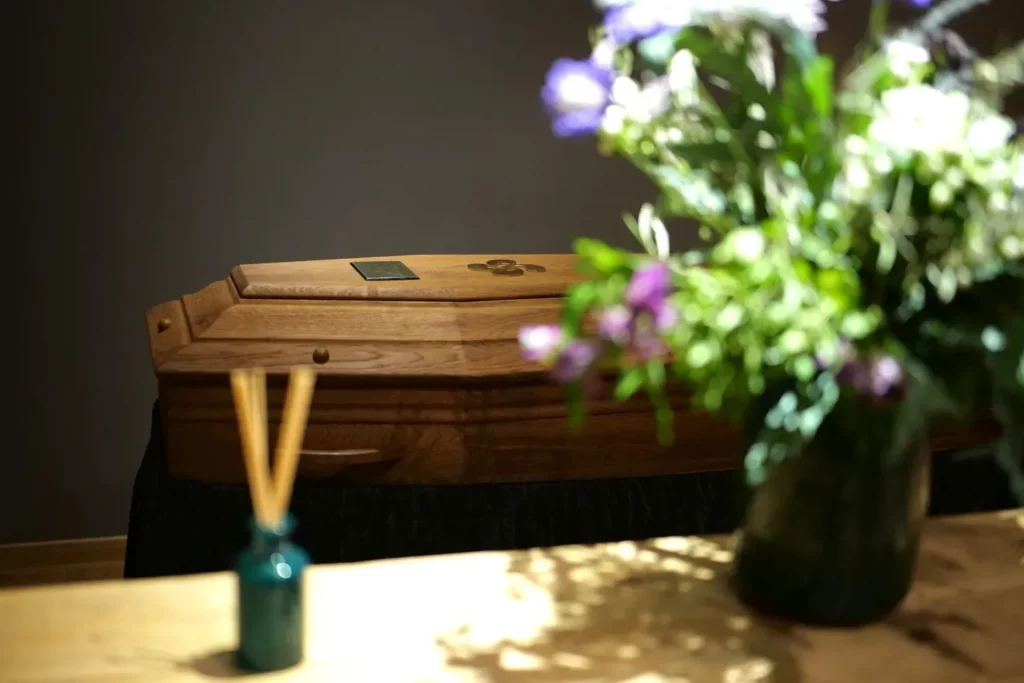 Chambre mortuaire avec cercueil en bois et bouquet de fleurs fraîches.